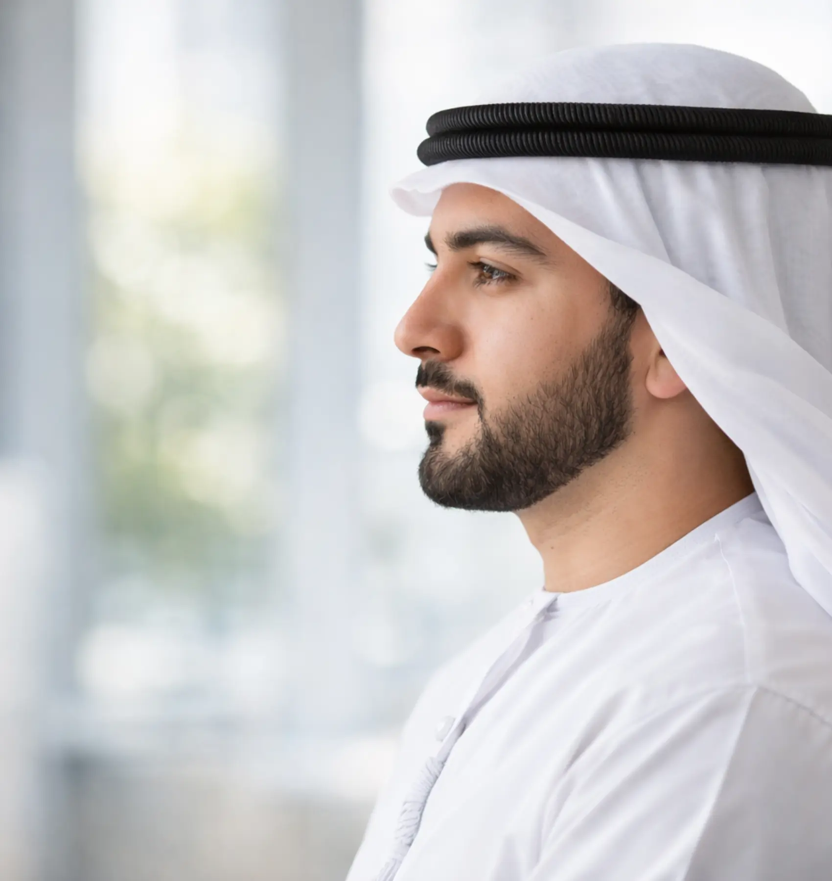 شهادة حية لرجل يرتدي الزي الخليجي ينظر بثقة من النافذة، يرمز إلى قصة نجاح وتجربة ملهمة.